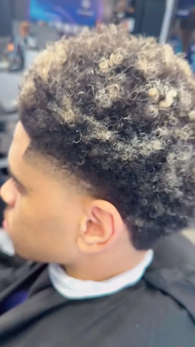 Volume bouclé conservé sur le dessus et dégradé court sur les côtés, chez Champions Barber