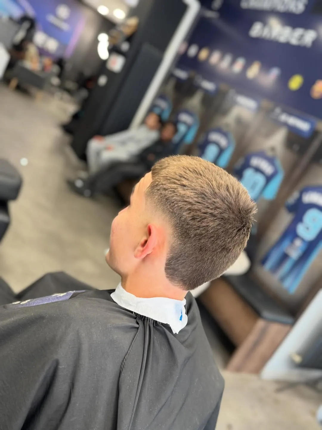 Coupe courte terminée devant les vitrines à maillots et l'affiche Champions Barber du salon