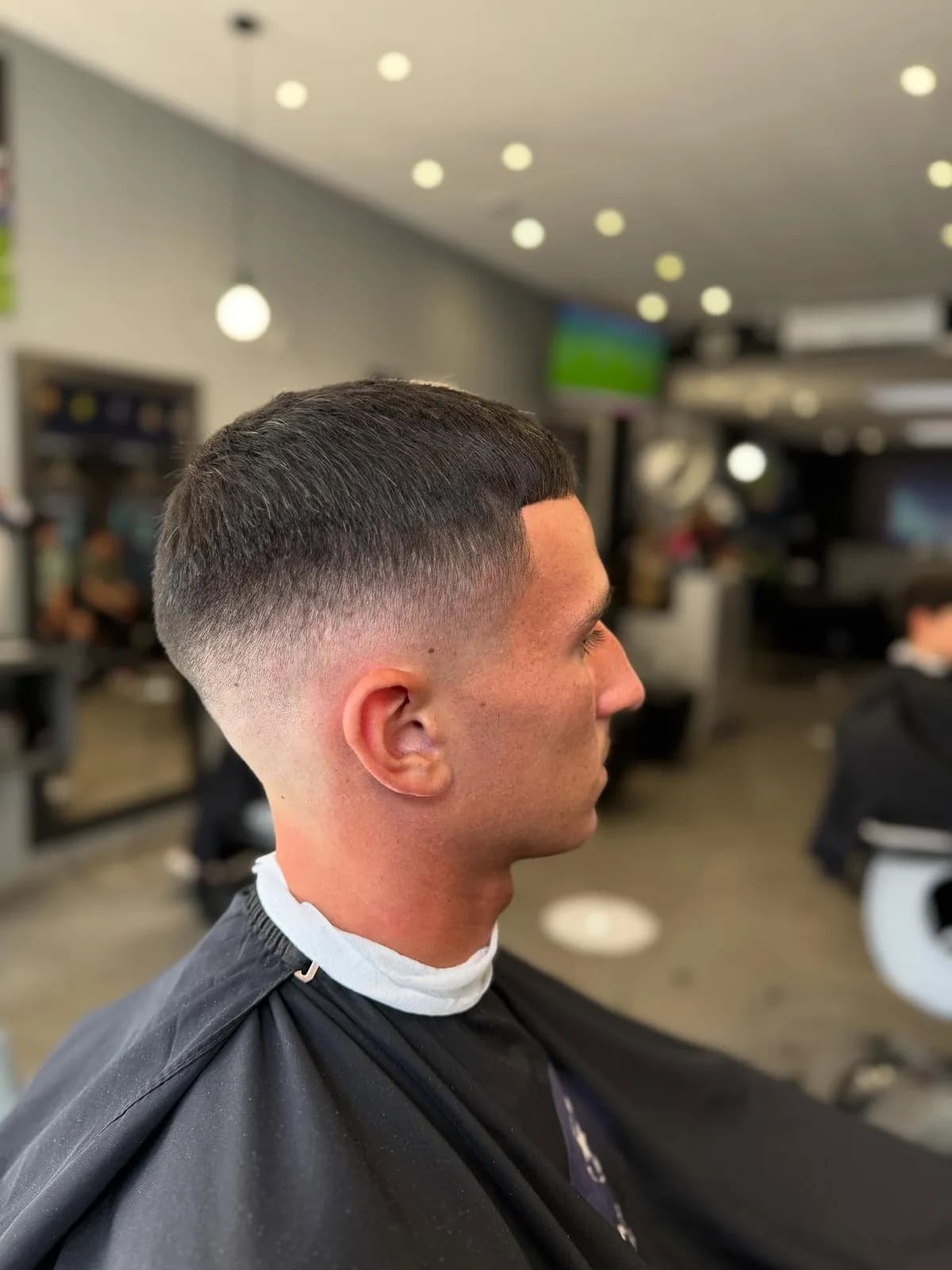 Dégradé court terminé chez Champions Barber, le salon et ses écrans en arrière-plan