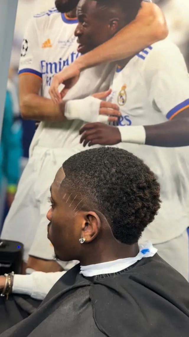 Coupe afro avec traits rasés et contours nets, devant la fresque du salon